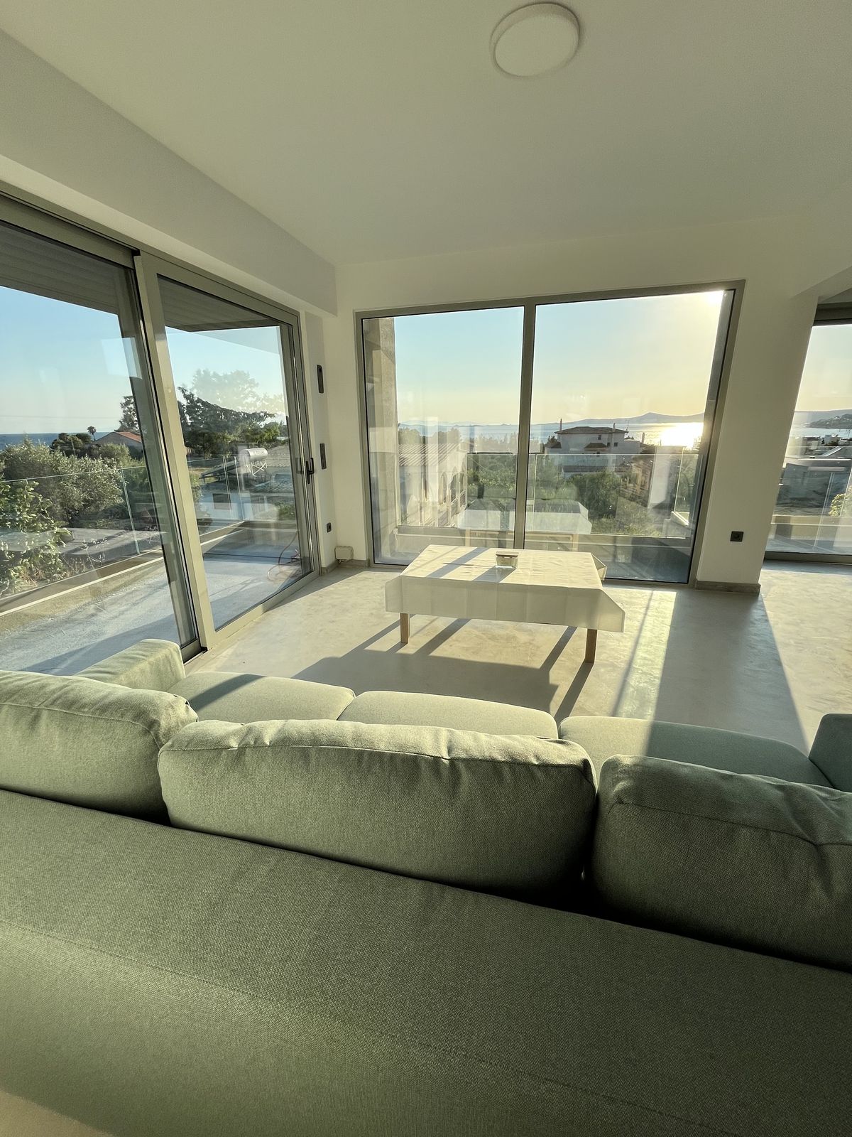 The sofa tucked into the glazed corner, the terrace and the bay beyond.
