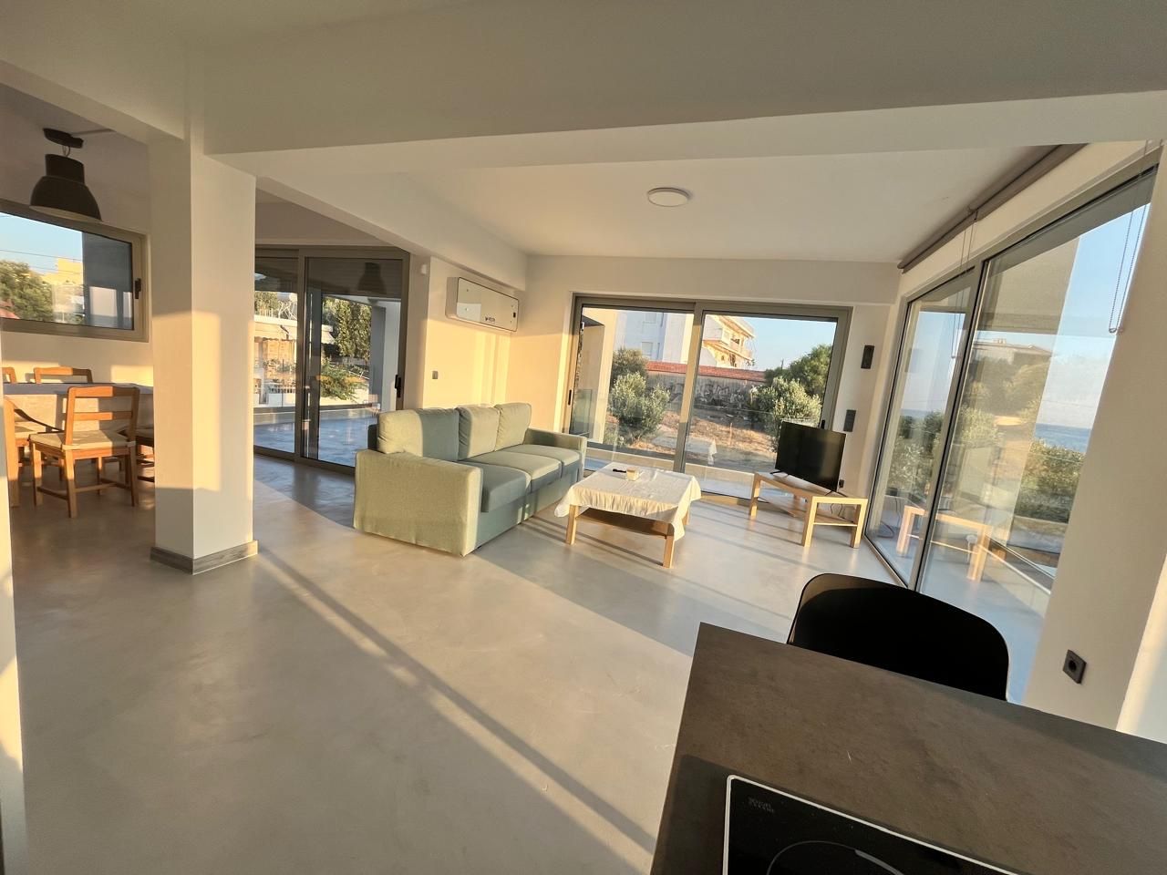 The open-plan living room, wrapped in glass with the coast beyond.