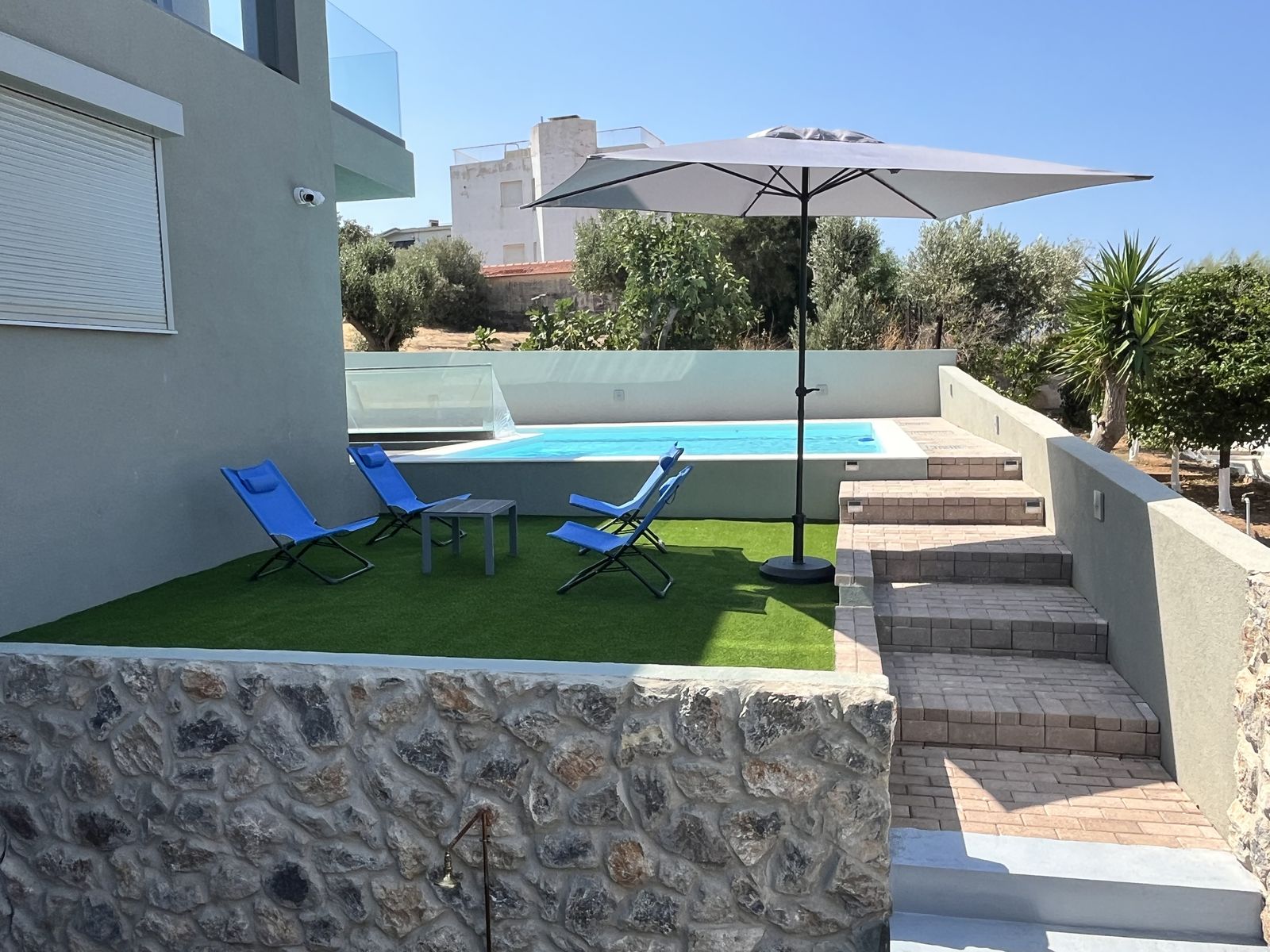The garden — sun loungers on the lawn beneath the umbrella, above the stone wall.