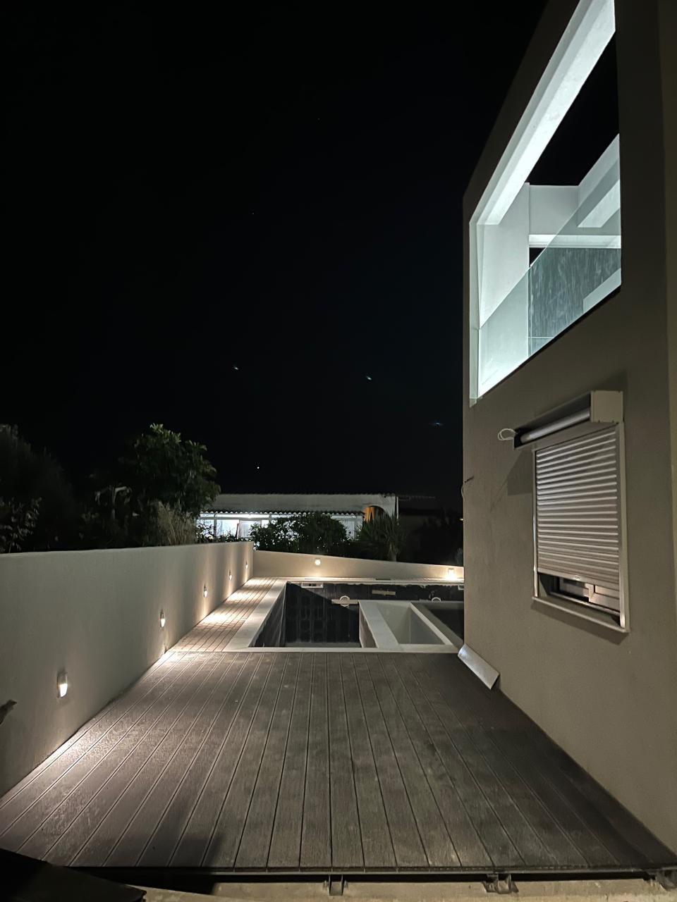 The pool deck and glass-walled upper floor of Blue Bay Dream A, lit at dusk.