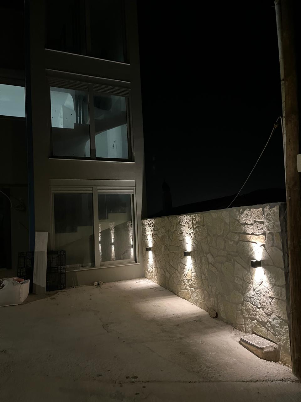 Natural-stone wall with warm uplighting beside the villa.