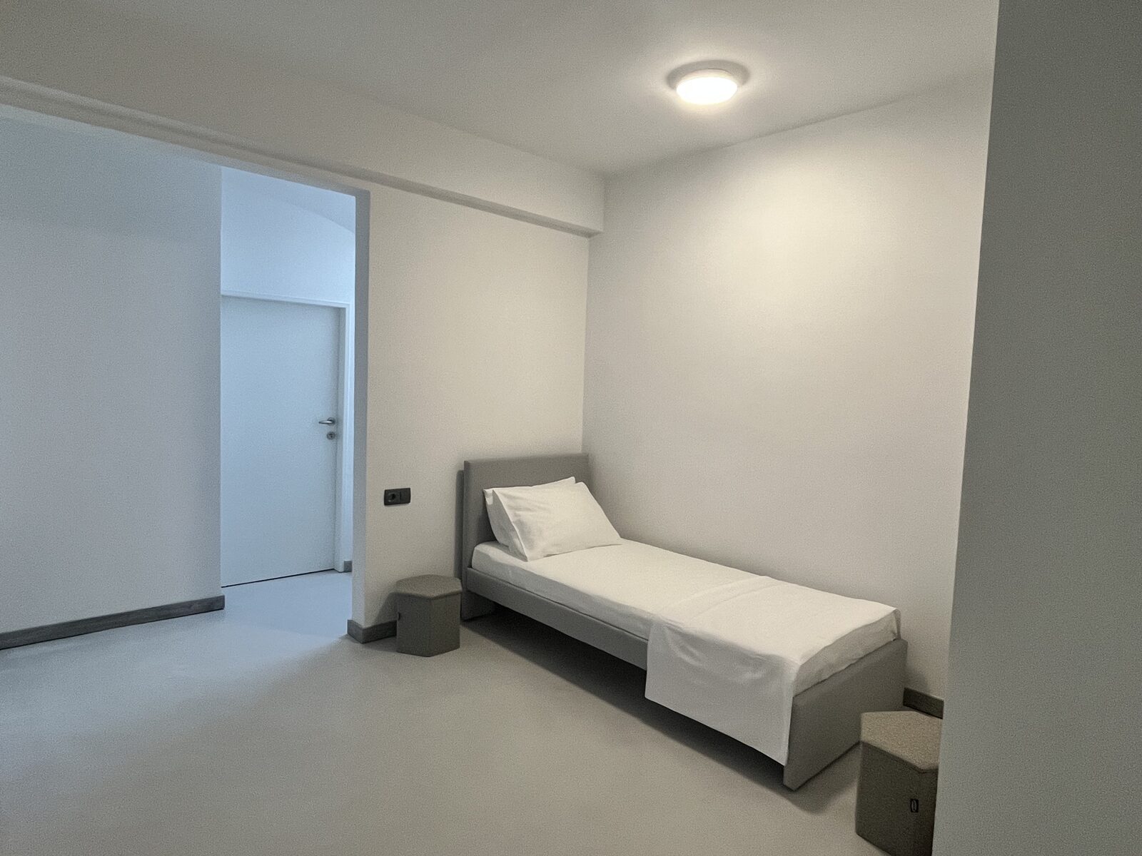 The single room off the hallway, made up in white with bedside stools either end.