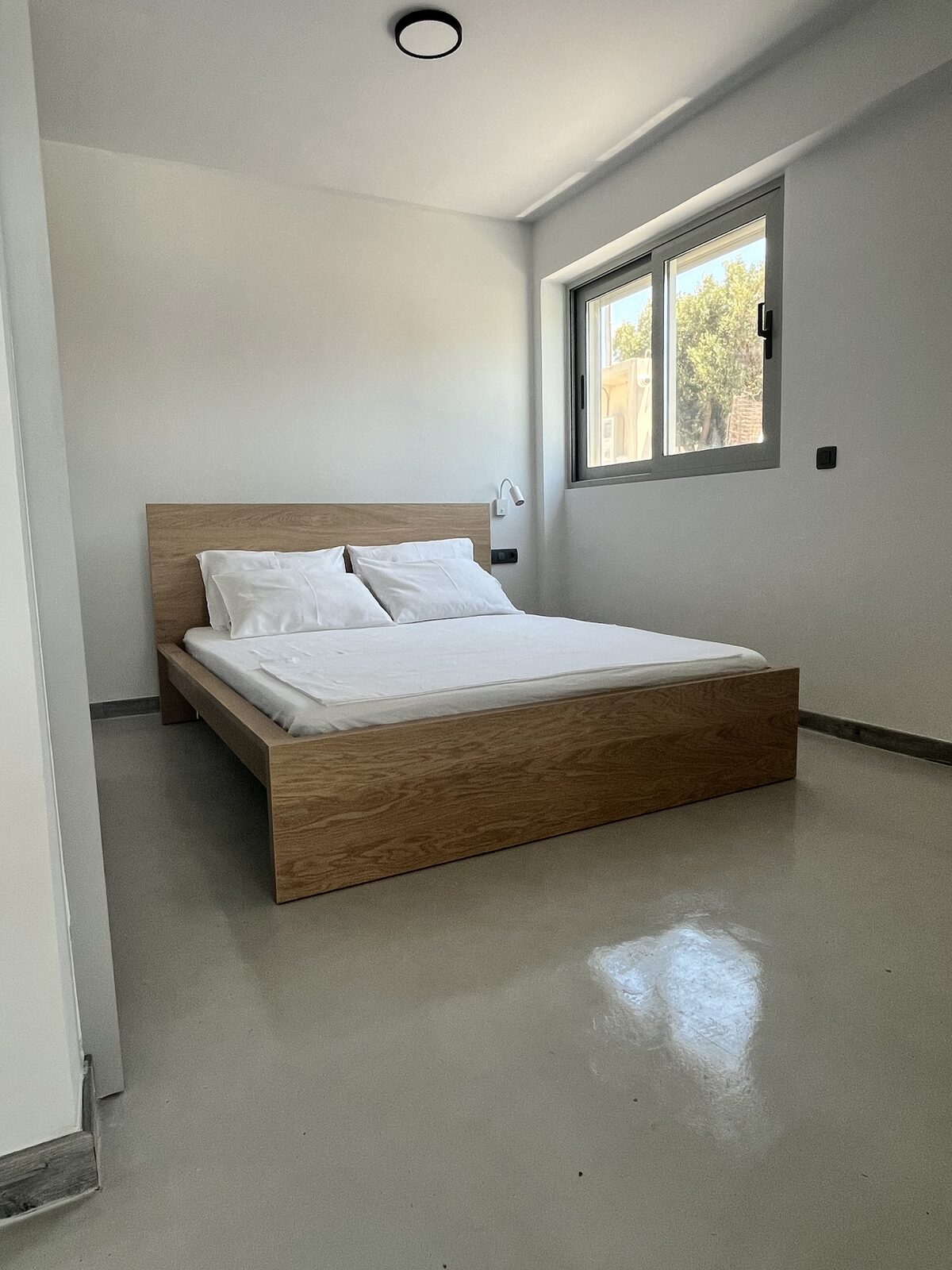 A further double bedroom, spare and bright, the bed set beside a window looking into the pines.