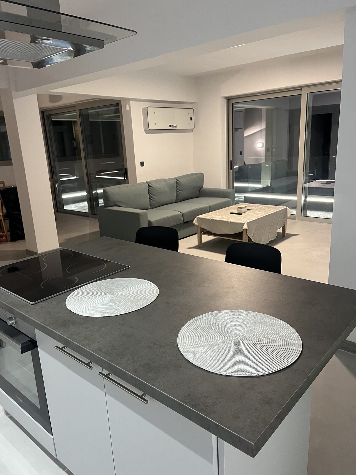 A kitchen counter in dark stone looking through to the sofa and the terrace doors beyond.